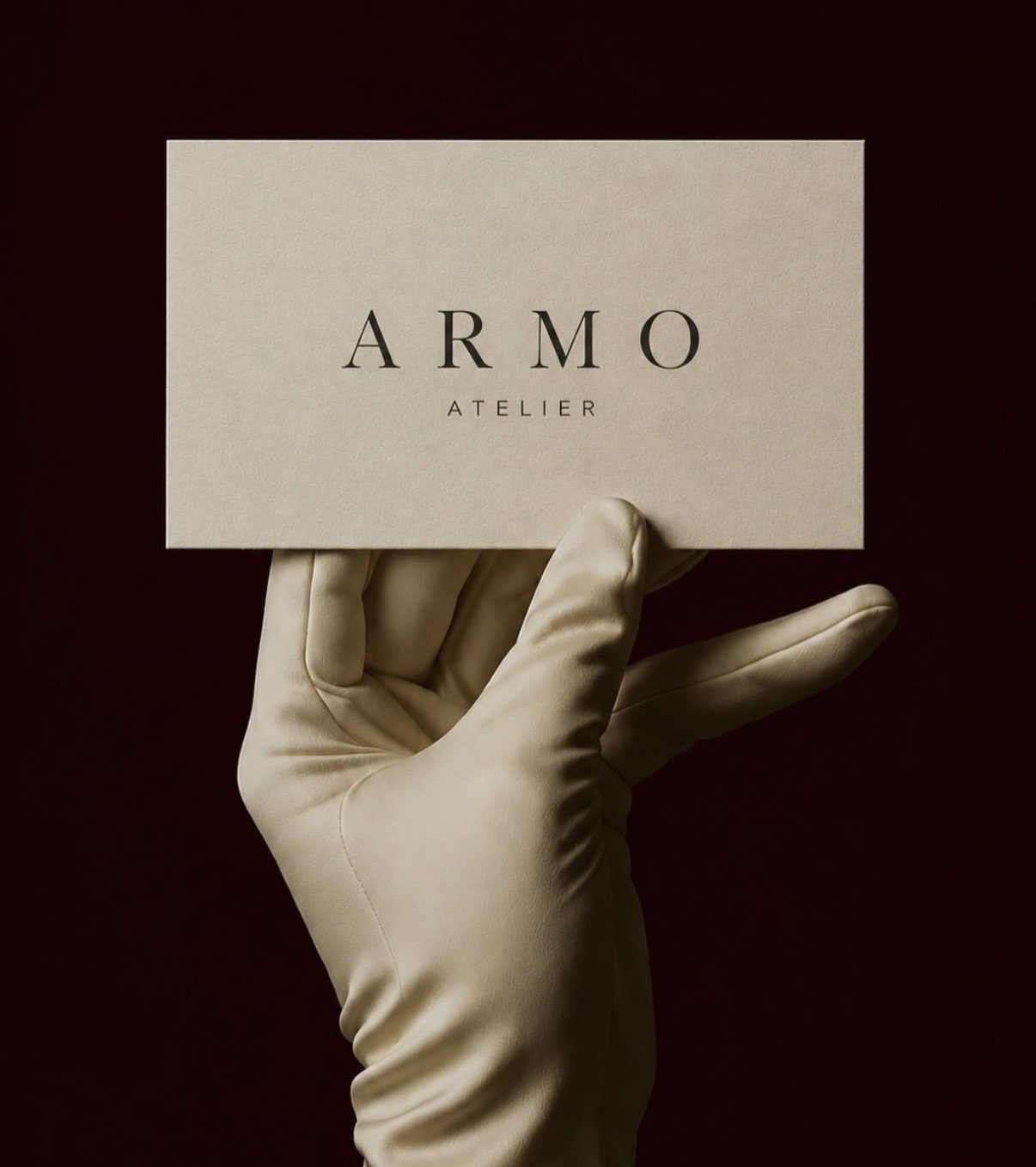 A hand in an ivory leather glove holding an Armo Atelier business card.