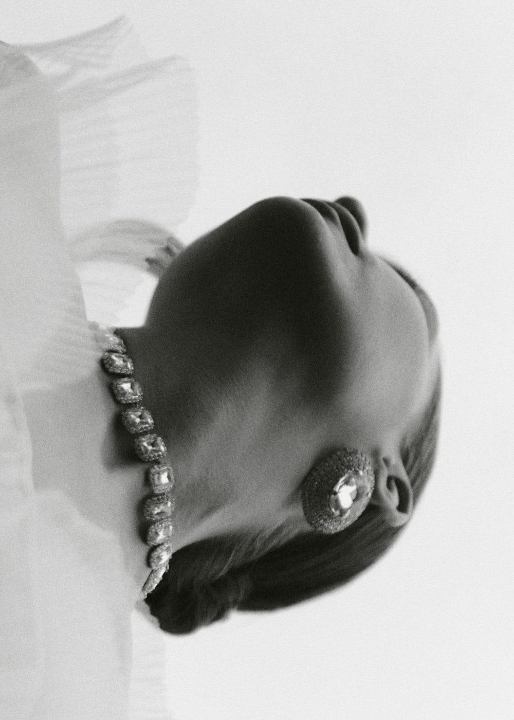 Black and white portrait of a woman with her head tipped back, wearing a crystal necklace and statement earring.